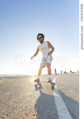 Man skateboards along the beachside path during sunset with warm light shining Man skateboards along the beachside path during sunset with warm light shining 142454406