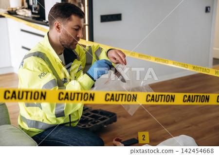 Police detective examining evidence at a murder scene, wearing a reflective jacket, with caution tape and a body outline visible on the floor Police detective examining evidence at a murder scene, wearing a reflective jacket, with caution tape and a body outline visible on the floor 142454668