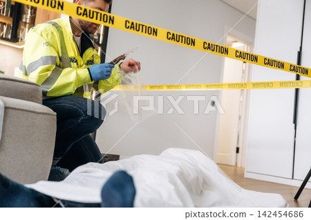Forensic expert in yellow police jacket collecting evidence at a murder scene, with caution tape and a covered body visible in a modern interior setting Forensic expert in yellow police jacket collecting evidence at a murder scene, with caution tape and a covered body visible in a modern interior setting 142454686