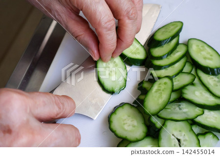 Close-up of an elderly woman's hands cutting a cucumber. Close-up of an elderly woman's hands cutting a cucumber. 142455014