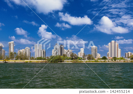 serene coastal cityscape with high-rise buildings and trees from water level, urban skyline with concrete, glass, and metal structures, real estate development, modern living, blue and gray. serene coastal cityscape with high-rise buildings and trees from water level, urban skyline with concrete, glass, and metal structures, real estate development, modern living, blue and gray. 142455214