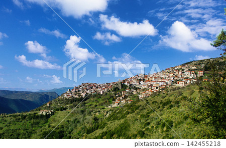 serene hillside village nestled in picturesque mountainous landscape with stone and wood houses and rooftops, aerial perspective showing greenery and blue skies. serene hillside village nestled in picturesque mountainous landscape with stone and wood houses and rooftops, aerial perspective showing greenery and blue skies. 142455218