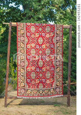 Traditional red Kotel carpet with ornamental floral and geometric pattern displayed outdoors in park Bulgaria. Bright Bulgarian textile heritage and handcrafted rug artistry Traditional red Kotel carpet with ornamental floral and geometric pattern displayed outdoors in park Bulgaria. Bright Bulgarian textile heritage and handcrafted rug artistry 142455281