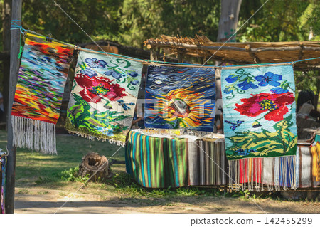 Colorful handmade carpets and woven rugs with floral and artistic patterns displayed outdoors at a traditional craft festival in Kotel, Bulgaria. Bulgarian textile heritage and folk craftsmanship Colorful handmade carpets and woven rugs with floral and artistic patterns displayed outdoors at a traditional craft festival in Kotel, Bulgaria. Bulgarian textile heritage and folk craftsmanship 142455299