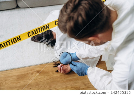 Forensic expert examining evidence at a murder scene, with a female victim lying on the floor and caution tape marking the area in a residential setting Forensic expert examining evidence at a murder scene, with a female victim lying on the floor and caution tape marking the area in a residential setting 142455335