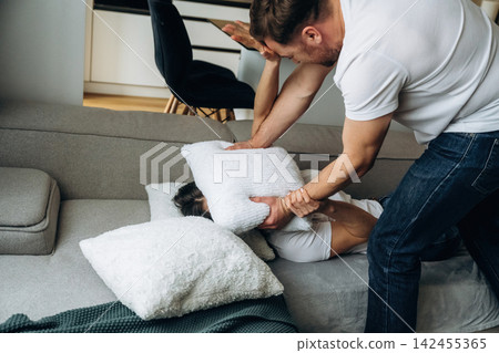 Man Silencing Woman With Pillow During Violent Domestic Dispute On Couch At Home Man Silencing Woman With Pillow During Violent Domestic Dispute On Couch At Home 142455365