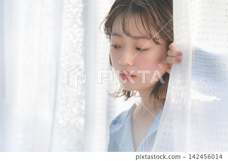 一個女人正透過窗簾的縫隙向外窺視。 一個女人正透過窗簾的縫隙向外窺視。 142456014