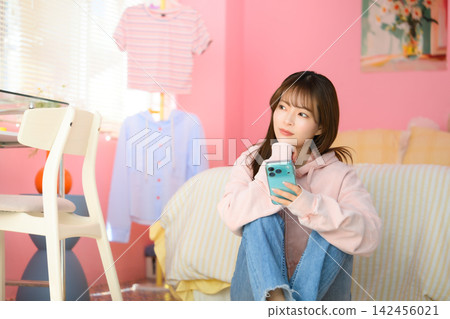 A woman holding a smartphone in a pink room A woman holding a smartphone in a pink room 142456021