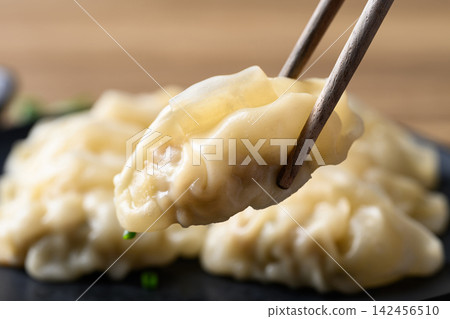 Close-up of dumpling stuffed with minced pork held by wooden chopsticks, Asian food Close-up of dumpling stuffed with minced pork held by wooden chopsticks, Asian food 142456510