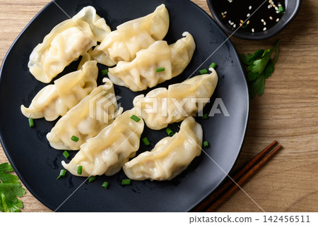 Dumpling stuffed with minced pork on black plate eaten with sesame oil dipping sauce Dumpling stuffed with minced pork on black plate eaten with sesame oil dipping sauce 142456511