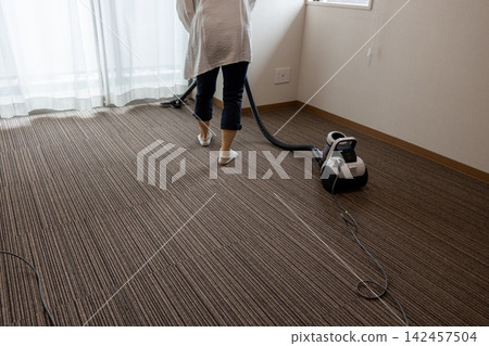 一位女士正在她的一房公寓裡吸塵。 一位女士正在她的一房公寓裡吸塵。 142457504