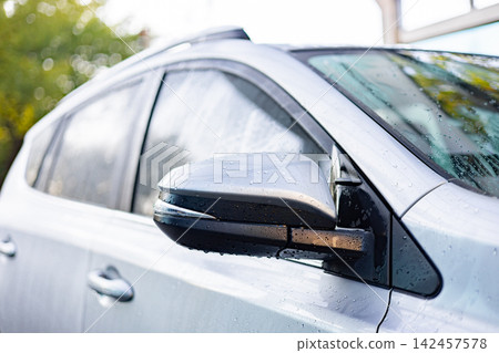 Close-up of a silver car's side mirror covered in water droplets after a wash or rain shower Close-up of a silver car's side mirror covered in water droplets after a wash or rain shower 142457578