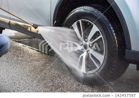 A person in jeans uses a pressure washer to clean the wheel and tire of a vehicle on a gravel surface A person in jeans uses a pressure washer to clean the wheel and tire of a vehicle on a gravel surface 142457597