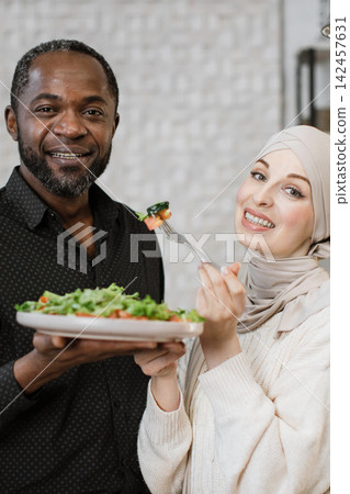 A smiling African man and a woman in a hijab share a healthy salad, highlighting togetherness and good food A smiling African man and a woman in a hijab share a healthy salad, highlighting togetherness and good food 142457631