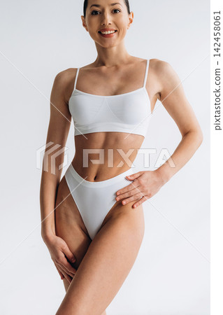 Slim female model in white lingerie poses confidently against a plain background, showcasing a toned physique and emphasizing body positivity and fitness aesthetics Slim female model in white lingerie poses confidently against a plain background, showcasing a toned physique and emphasizing body positivity and fitness aesthetics 142458061