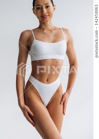 Slim female model in white bikini poses confidently against a light background, showcasing a toned physique and emphasizing body positivity and fitness aesthetics Slim female model in white bikini poses confidently against a light background, showcasing a toned physique and emphasizing body positivity and fitness aesthetics 142458063