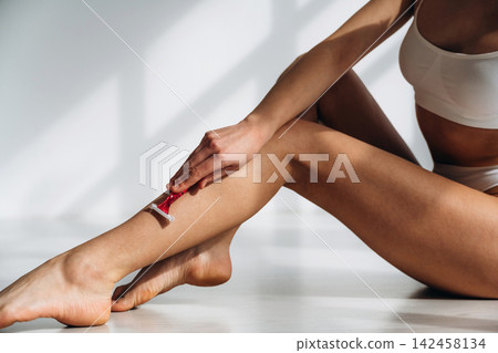 Female model shaving her leg with a razor in a bright indoor setting, showcasing smooth skin and a healthy lifestyle focus on personal grooming and beauty care Female model shaving her leg with a razor in a bright indoor setting, showcasing smooth skin and a healthy lifestyle focus on personal grooming and beauty care 142458134