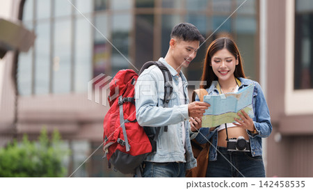 Asian couple looking at paper map while travelling outdoors in city for tourism Asian couple looking at paper map while travelling outdoors in city for tourism 142458535