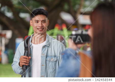 Asian man posing for photo taken by friend outdoors for travel lifestyle Asian man posing for photo taken by friend outdoors for travel lifestyle 142458544