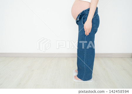 Pregnant woman with big belly standing on weight scale at home. Healthy weight gain during pregnancy avoid pregnancy complications such as gestational diabetes, preeclampsia, and cesarean delivery. Pregnant woman with big belly standing on weight scale at home. Healthy weight gain during pregnancy avoid pregnancy complications such as gestational diabetes, preeclampsia, and cesarean delivery. 142458594