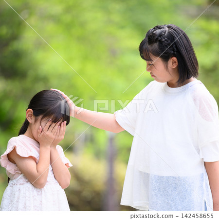 An older sister strokes the head of her crying younger sister outdoors. An older sister strokes the head of her crying younger sister outdoors. 142458655