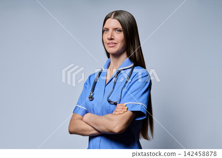 Three-quarter portrait of confident female nurse standing with folded arms on grey background Three-quarter portrait of confident female nurse standing with folded arms on grey background 142458878
