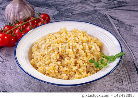 Bulgur wheat in white bowl with cherry tomatoes and garlic on rustic surface Bulgur wheat in white bowl with cherry tomatoes and garlic on rustic surface 142458893