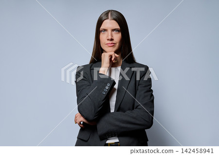 Confident businesswoman with hand on chin looking at camera against grey background Confident businesswoman with hand on chin looking at camera against grey background 142458941