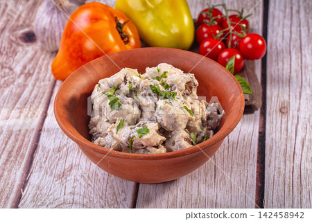 Rustic clay bowl of meatballs in creamy sauce with fresh vegetables on wooden table 142458942