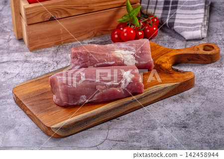 Raw pork tenderloin on wooden cutting board with fresh cherry tomatoes 142458944