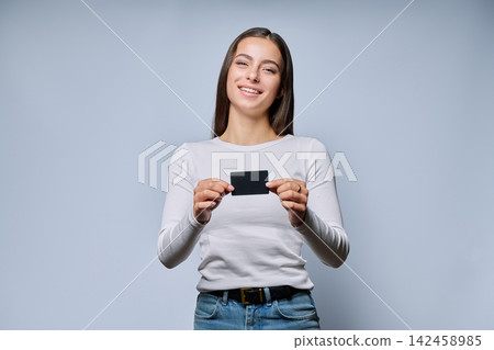Smiling woman holding black plastic transport card on grey background Smiling woman holding black plastic transport card on grey background 142458985