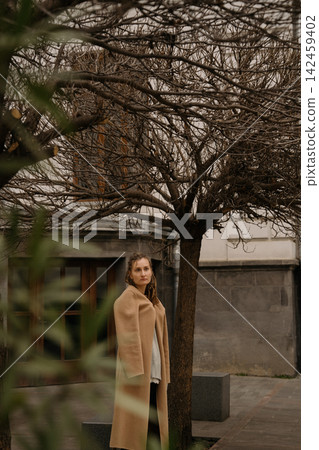 Girl with dreadlocks stands by bare trees in urban area on a cloudy day Girl with dreadlocks stands by bare trees in urban area on a cloudy day 142459402