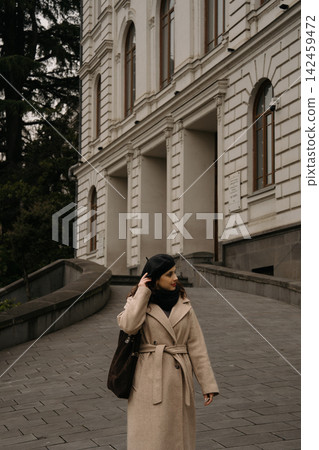 Woman wearing beret walks along sidewalk near building in urban area during cool weather Woman wearing beret walks along sidewalk near building in urban area during cool weather 142459472
