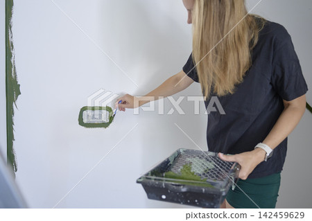 Woman applies green paint around masked electrical outlet with small brush Woman applies green paint around masked electrical outlet with small brush 142459629