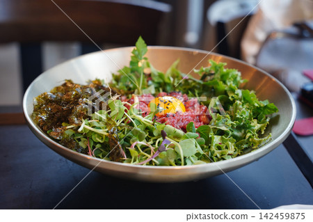Traditional Korean raw beef tartare bibimbap with egg yolk and fresh vegetables served in a luxury brass bowl close-up Traditional Korean raw beef tartare bibimbap with egg yolk and fresh vegetables served in a luxury brass bowl close-up 142459875