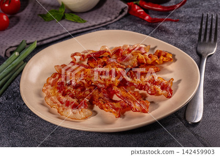 Crispy fried bacon strips on plate with fork and vegetables Crispy fried bacon strips on plate with fork and vegetables 142459903