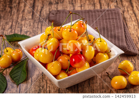 Yellow cherries in white bowl on rustic wooden table with green leaves Yellow cherries in white bowl on rustic wooden table with green leaves 142459913