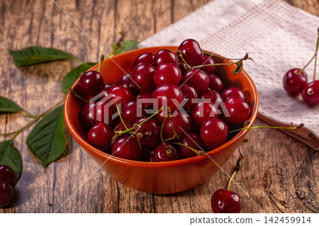 Fresh red cherries in orange bowl on rustic wooden table with green leaves Fresh red cherries in orange bowl on rustic wooden table with green leaves 142459914