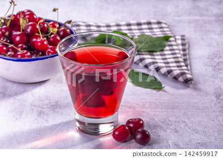 Glass of red cherry juice with fresh cherries and checkered napkin on textured surface 142459917