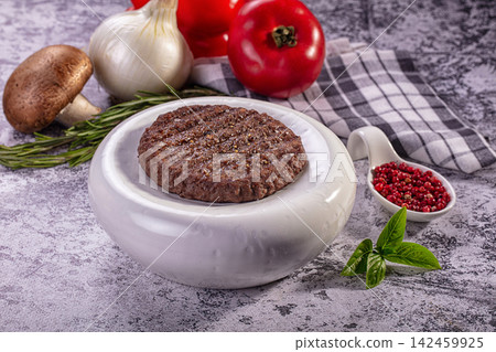 Raw beef patty in white bowl with fresh vegetables and herbs on rustic surface Raw beef patty in white bowl with fresh vegetables and herbs on rustic surface 142459925