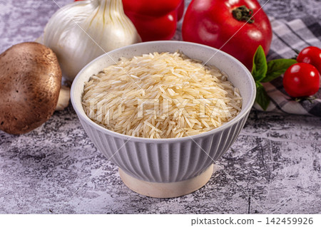 Bowl of uncooked rice with fresh vegetables on rustic surface Bowl of uncooked rice with fresh vegetables on rustic surface 142459926