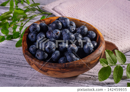 Fresh blueberries in wooden bowl with green leaves on rustic white wood 142459935