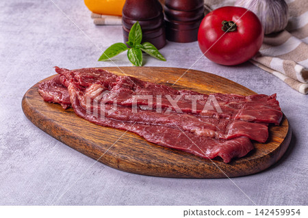 Raw beef steak slices on wooden cutting board with tomato basil and pepper mills 142459954