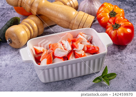 Chopped surimi crab sticks in white ceramic dish with tomatoes garlic and wooden pepper mills on textured gray surface Chopped surimi crab sticks in white ceramic dish with tomatoes garlic and wooden pepper mills on textured gray surface 142459970