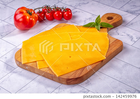 Sliced cheddar cheese on wooden cutting board with tomato and basil Sliced cheddar cheese on wooden cutting board with tomato and basil 142459976