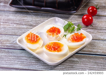 Deviled eggs topped with red caviar on white plate with cherry tomatoes and microgreens 142459993