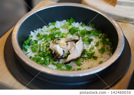 Premium Korean abalone rice with pine mushrooms and chives cooked in a traditional iron pot, healthy stamina food close-up Premium Korean abalone rice with pine mushrooms and chives cooked in a traditional iron pot, healthy stamina food close-up 142460038