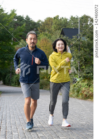 一對夫婦沿著林蔭大道跑步,周圍環繞著秋葉。 一對夫婦沿著林蔭大道跑步,周圍環繞著秋葉。 142460072