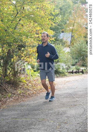 A man running through a villa area in autumn. Running, jogging. 142460078
