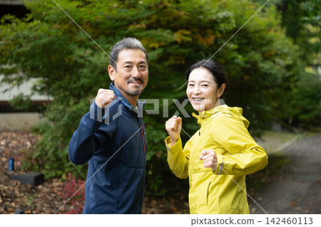 A middle-aged couple celebrates their run/jogging by striking a victory pose. A middle-aged couple celebrates their run/jogging by striking a victory pose. 142460113